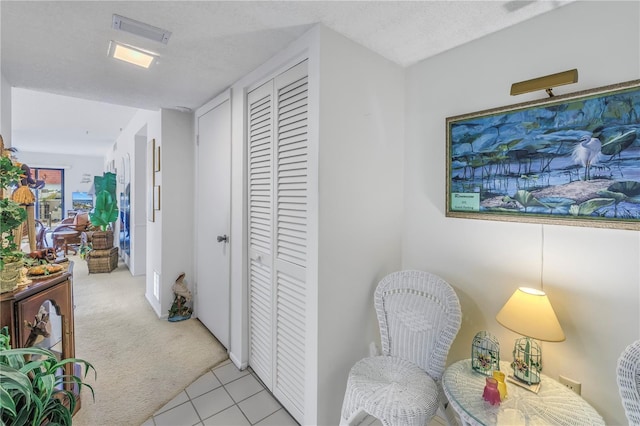 hall featuring light tile patterned flooring, visible vents, a textured ceiling, and light colored carpet