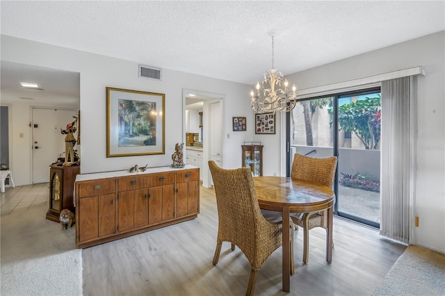 dining space with a textured ceiling, light wood-type flooring, visible vents, and a notable chandelier