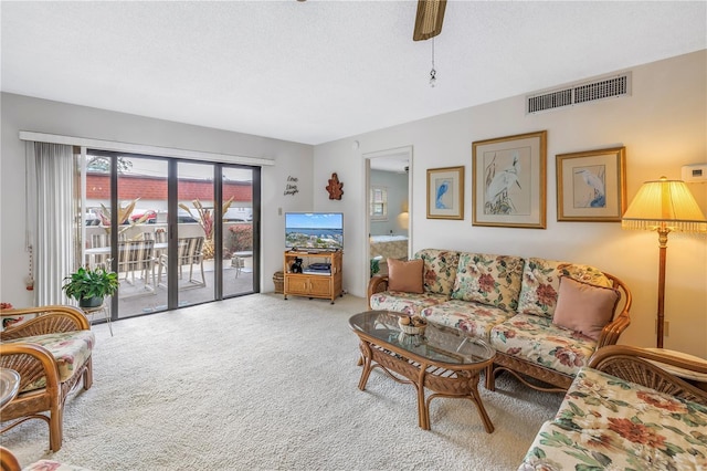 living area with a textured ceiling, carpet flooring, visible vents, and a ceiling fan