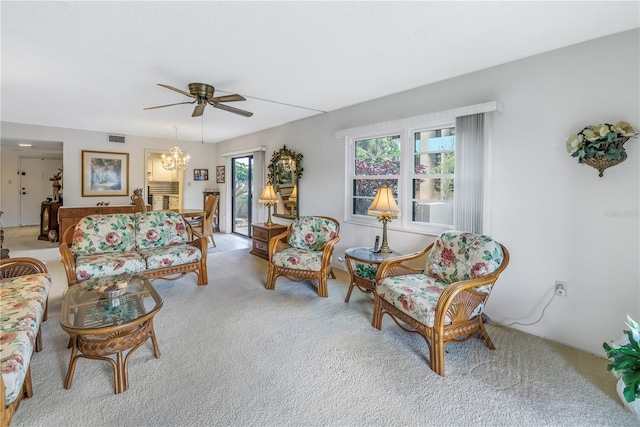 living area featuring ceiling fan with notable chandelier, visible vents, and light colored carpet