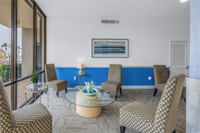 sitting room with a textured ceiling, a wall of windows, visible vents, and baseboards