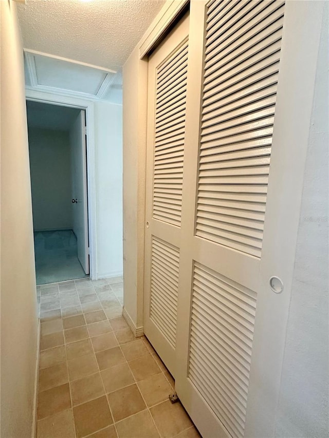 hall featuring light tile patterned floors, attic access, and a textured ceiling