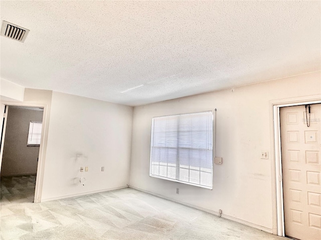 spare room featuring a textured ceiling, baseboards, visible vents, and light colored carpet