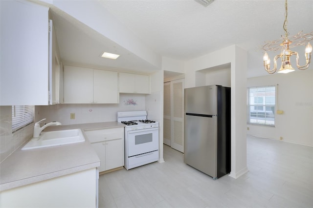 kitchen featuring a notable chandelier, a sink, white gas range, freestanding refrigerator, and backsplash
