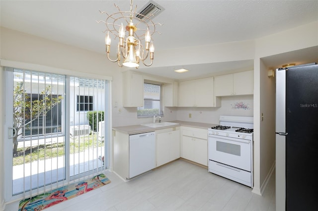 kitchen with white appliances, light countertops, white cabinetry, a sink, and a notable chandelier