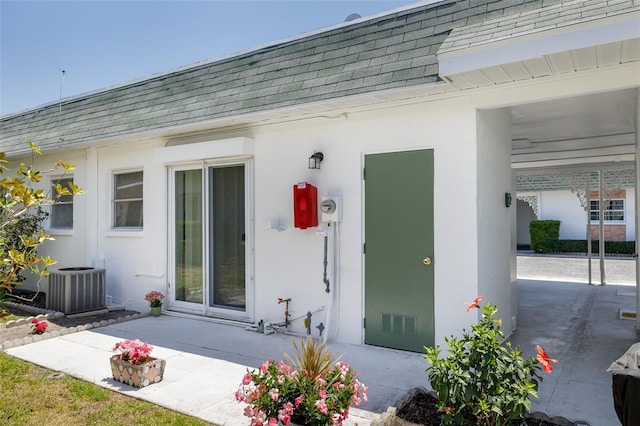 property entrance with cooling unit, a shingled roof, and visible vents
