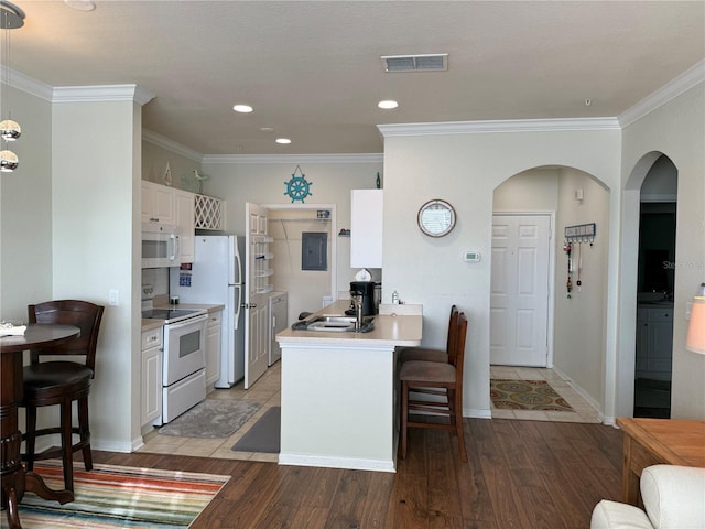 kitchen with light wood finished floors, visible vents, white appliances, a peninsula, and a kitchen breakfast bar