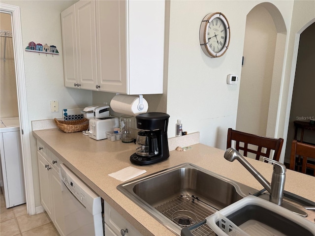 kitchen with arched walkways, white dishwasher, light countertops, white cabinetry, and a sink