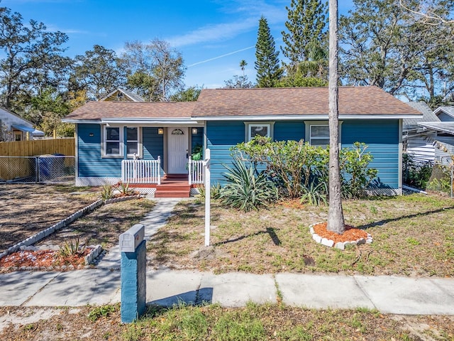 ranch-style house with a porch, roof with shingles, and fence