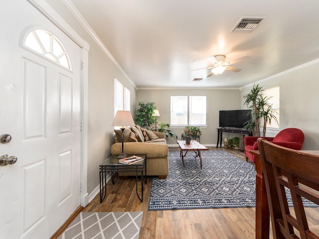 living area with baseboards, visible vents, a ceiling fan, ornamental molding, and wood finished floors