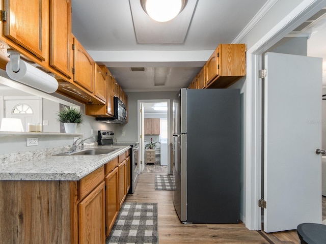 kitchen featuring a sink, light countertops, appliances with stainless steel finishes, light wood-type flooring, and brown cabinetry