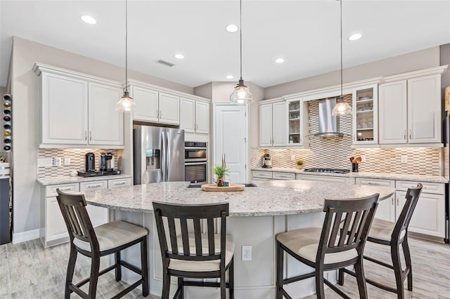 kitchen with stainless steel appliances, wall chimney range hood, light wood-type flooring, and white cabinetry