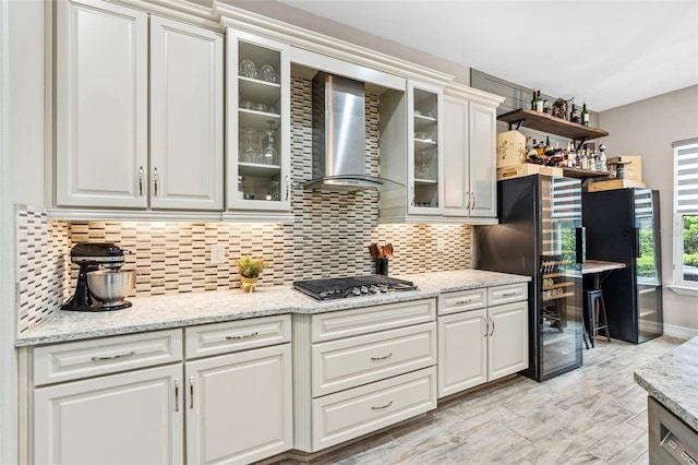 kitchen with wall chimney exhaust hood, stainless steel gas stovetop, white cabinetry, and tasteful backsplash