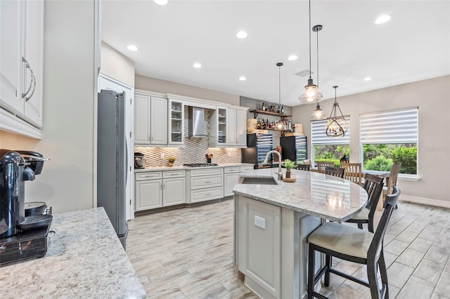 kitchen featuring decorative backsplash, appliances with stainless steel finishes, a kitchen breakfast bar, wall chimney range hood, and a sink