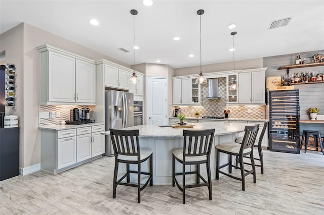 kitchen with a breakfast bar area, beverage cooler, visible vents, and wall chimney exhaust hood