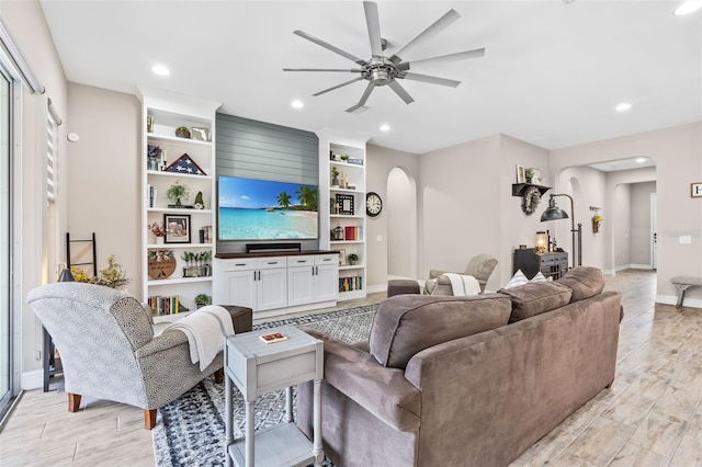 living area with arched walkways, ceiling fan, light wood-style flooring, and baseboards