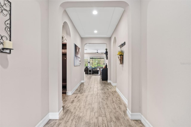 hall featuring light wood-type flooring, baseboards, arched walkways, and recessed lighting