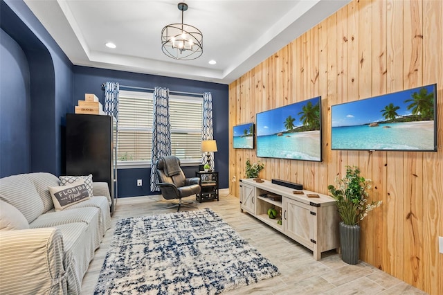 living room featuring light wood-style flooring, recessed lighting, wood walls, a tray ceiling, and an inviting chandelier