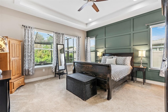 bedroom with baseboards, a raised ceiling, a ceiling fan, light colored carpet, and a decorative wall