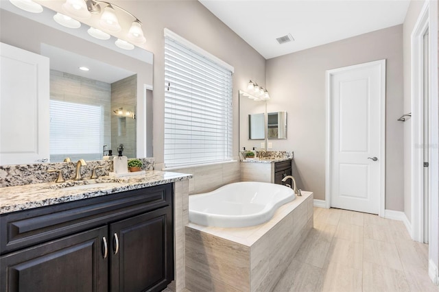 full bath featuring a garden tub, two vanities, a sink, visible vents, and a stall shower