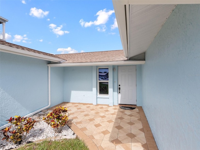 doorway to property with a shingled roof, a patio, and stucco siding