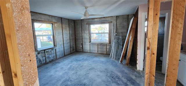 spare room featuring a wealth of natural light, ceiling fan, and unfinished concrete flooring