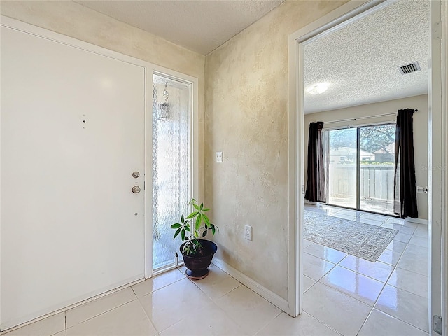 foyer entrance with light tile patterned floors, visible vents, a textured wall, a textured ceiling, and baseboards