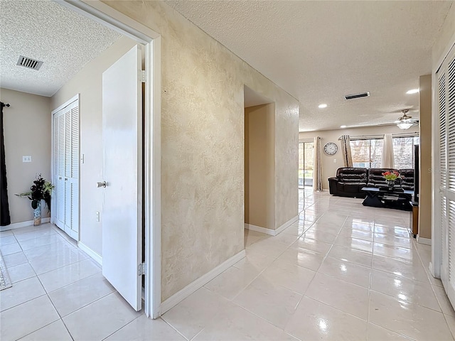 hallway with visible vents, a textured wall, a textured ceiling, and light tile patterned floors