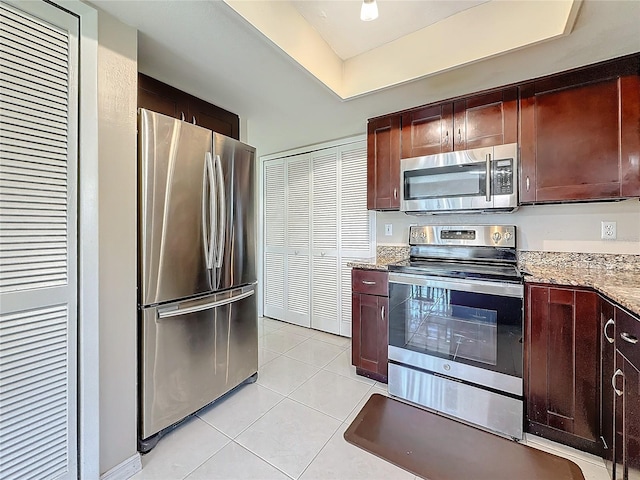 kitchen featuring stainless steel appliances, a raised ceiling, light tile patterned flooring, and light stone countertops