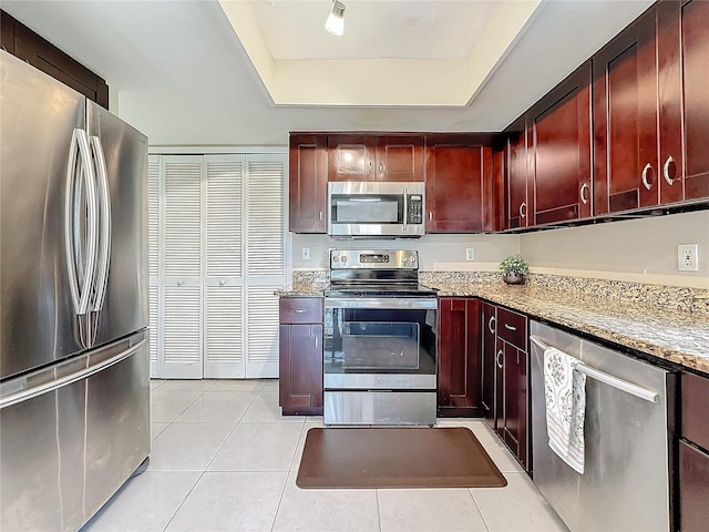 kitchen with light stone counters, a tray ceiling, stainless steel appliances, dark brown cabinets, and light tile patterned flooring