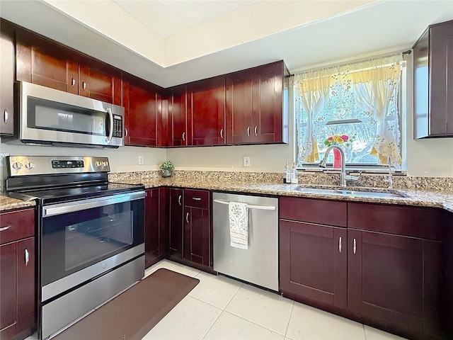 kitchen with light tile patterned floors, light stone counters, a sink, dark brown cabinets, and appliances with stainless steel finishes