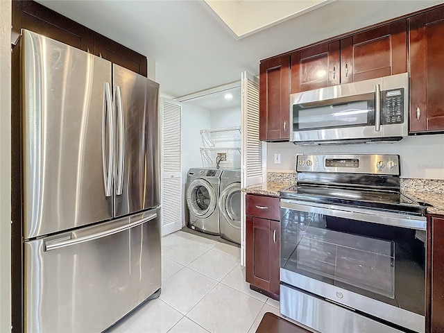 kitchen with reddish brown cabinets, washer and clothes dryer, light tile patterned floors, stainless steel appliances, and light stone countertops