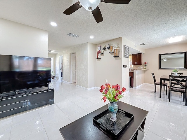 living area featuring a textured ceiling, light tile patterned flooring, visible vents, and baseboards