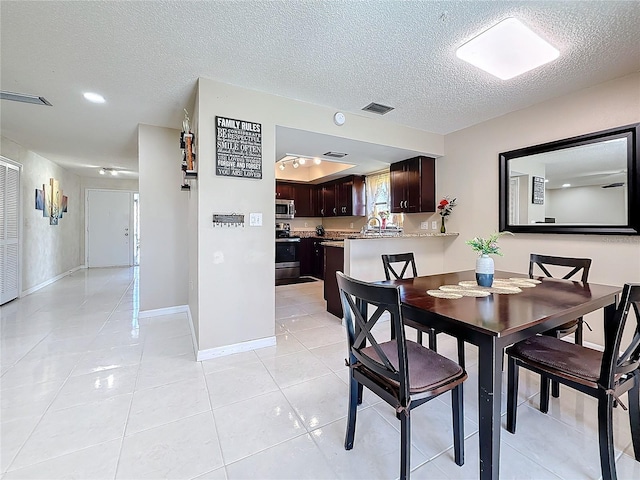 dining space featuring light tile patterned floors, a textured ceiling, visible vents, and baseboards