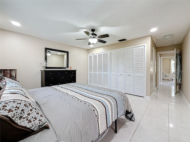 bedroom featuring a textured ceiling, light tile patterned flooring, visible vents, multiple closets, and a ceiling fan