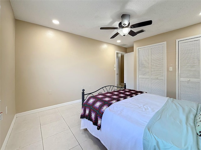 bedroom with light tile patterned floors, a textured ceiling, baseboards, and two closets