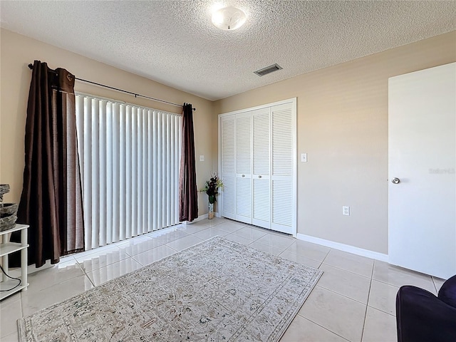 unfurnished bedroom featuring light tile patterned floors, baseboards, visible vents, and a textured ceiling