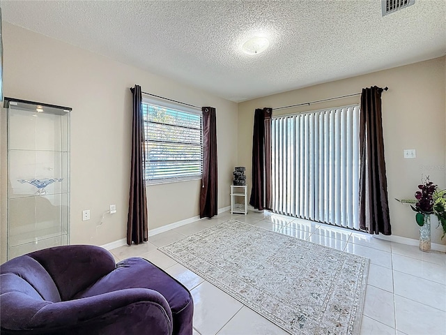 living area featuring a textured ceiling, light tile patterned flooring, visible vents, and baseboards