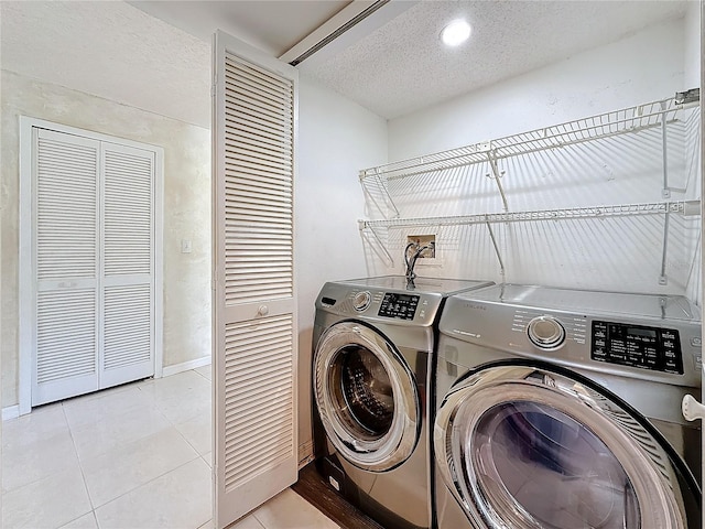 laundry area with a textured ceiling, separate washer and dryer, light tile patterned floors, and baseboards