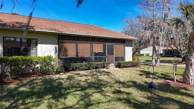 rear view of house featuring a sunroom, a shingled roof, a lawn, and stucco siding