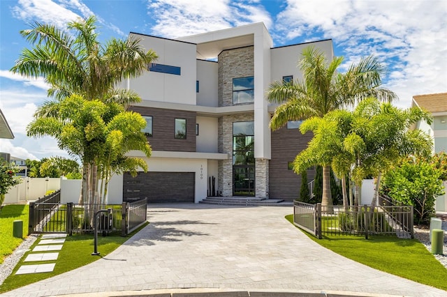 contemporary house with stone siding, a fenced front yard, a gate, decorative driveway, and stucco siding