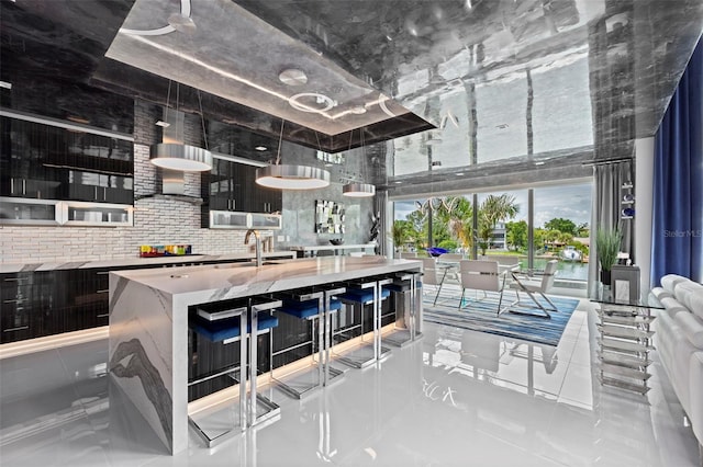 kitchen featuring a center island with sink, white microwave, light countertops, a sink, and light tile patterned flooring