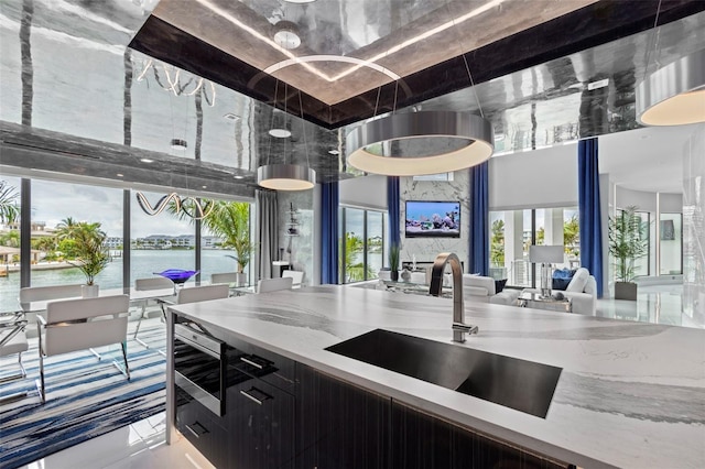 kitchen with light stone counters, a water view, a sink, a towering ceiling, and dark cabinetry