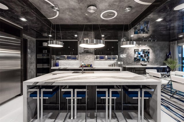 kitchen featuring tasteful backsplash, built in fridge, a center island with sink, and a sink