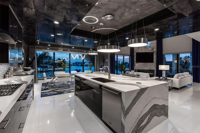 kitchen with modern cabinets, light stone counters, hanging light fixtures, a large island with sink, and a sink