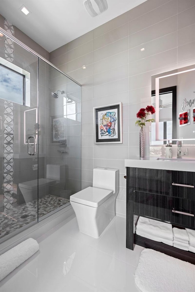 bathroom featuring toilet, tile patterned floors, vanity, a shower stall, and tile walls