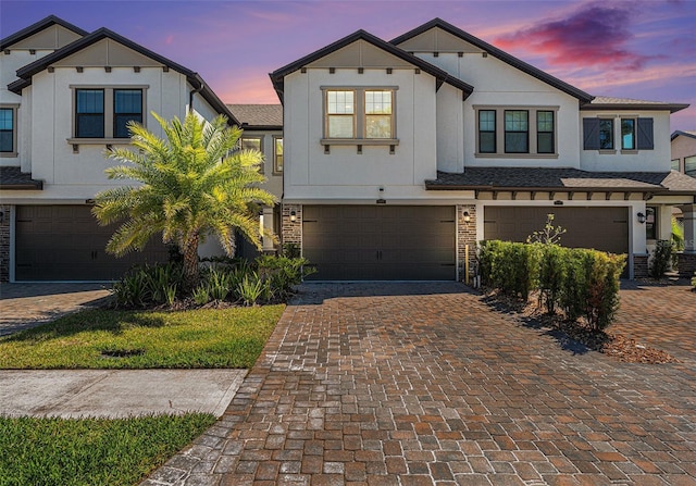 view of front of home featuring decorative driveway, brick siding, an attached garage, and stucco siding