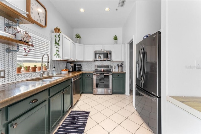 kitchen featuring stainless steel appliances, a sink, white cabinetry, backsplash, and green cabinetry