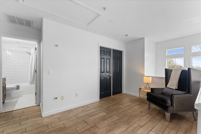 sitting room with baseboards, attic access, visible vents, and wood finished floors