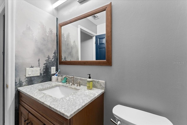 bathroom featuring toilet, a textured wall, visible vents, and vanity